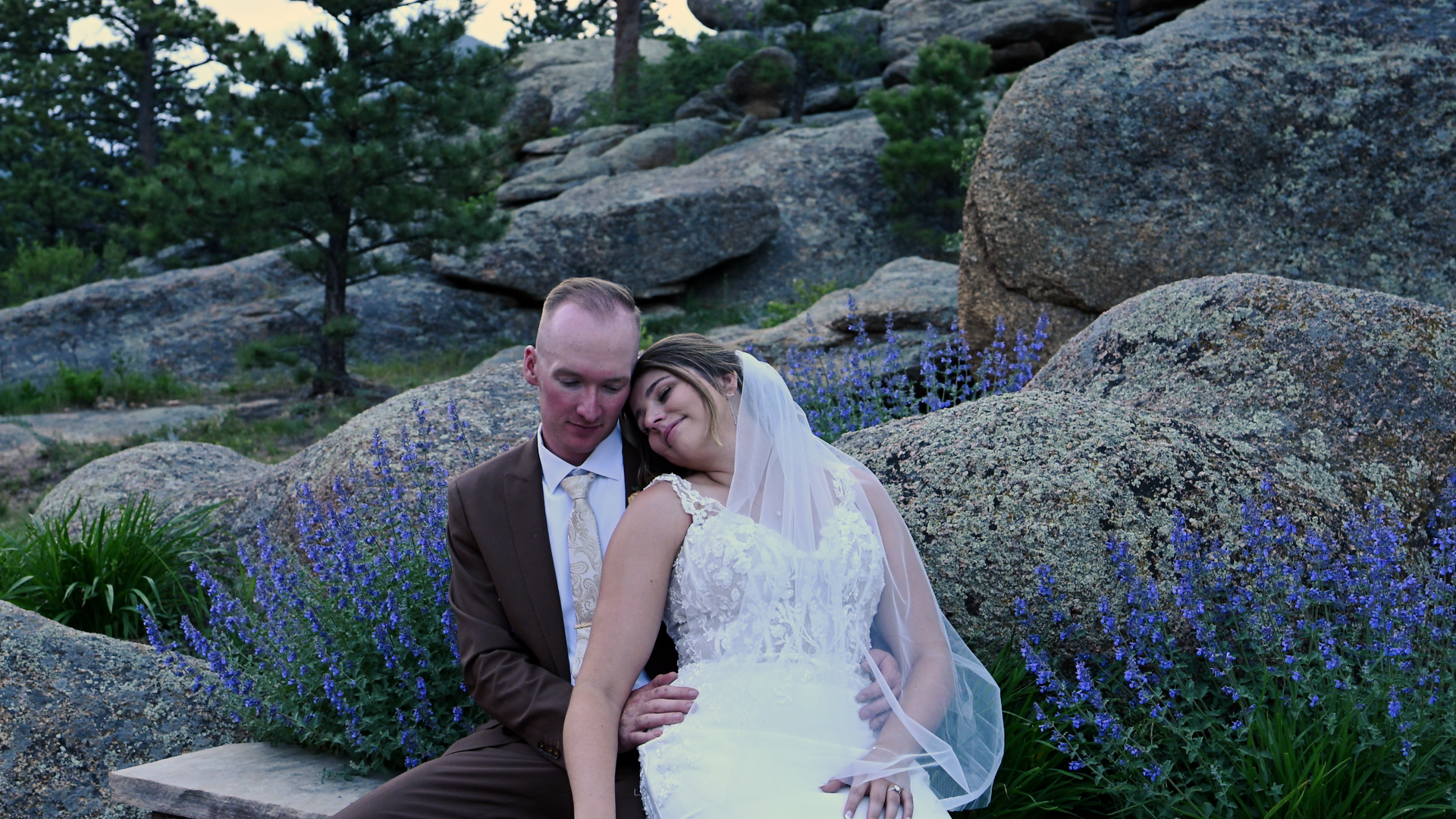 a newly married couple sitting on a bench amongst wildflowers on the evening of their wedding 